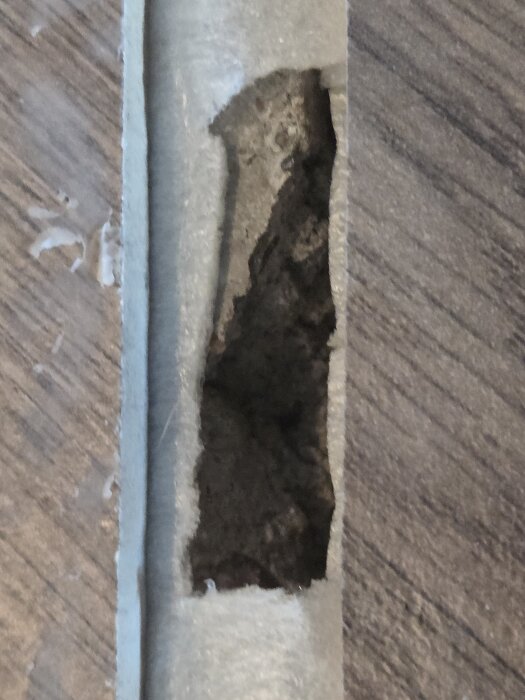 Skadat golv med hål i betongskiktet under en övergångslist i ett gammalt hus.