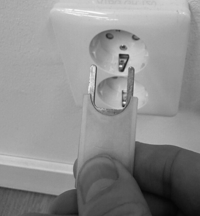 Spänningsprovare hålls framför ett vägguttag, används för att indikera spänning och fjärrstyra gruppsäkringen, men saknar jordningstestfunktion.