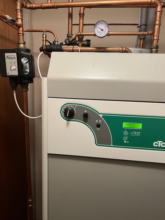 CTC-panna med kopparrör och termometer, i ett rum med värmesystem. Altech-komponent och elektronisk kontrollpanel syns.