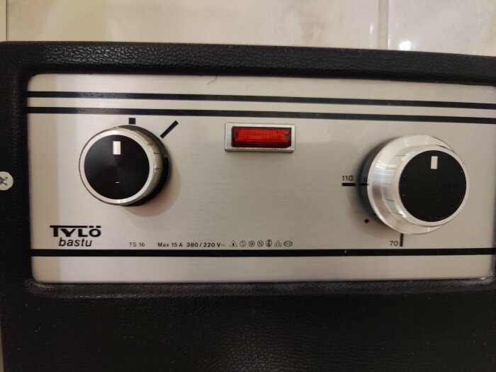 Kontrollpanel för en Tylo bastu med två rattar och en röd indikatorlampa, utan timer-markeringar.