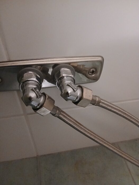 Ballofixer monterade på ett väggfäste i ett badrum med två anslutna flexibla metallslangar.