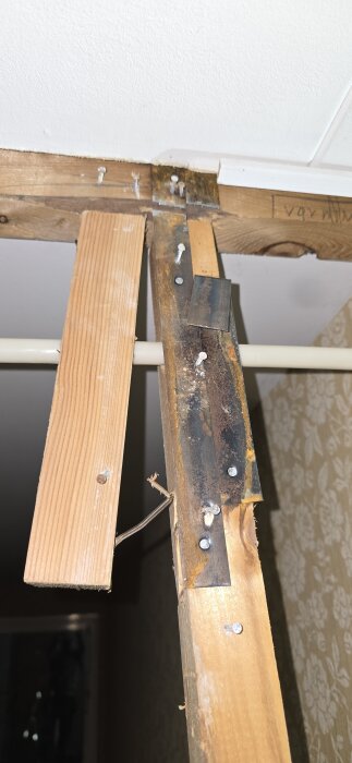 Träreglar med metallförstärkningar och rostiga spikar sitter i en takkonstruktion. Texten "varning" syns delvis på regeln.