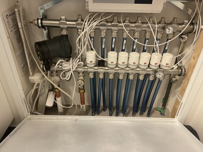 Golvvärmeslingor med kopplingar och mätare i ett skåp, del av ett frånluftsvärmesystem.