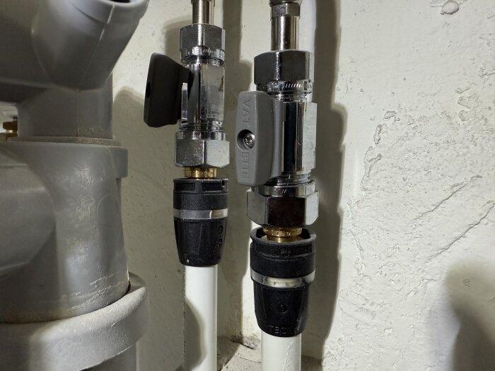 Rörkopplingar med muttrar och ventiler i en vägg, del av ett VVS-system. Kopplingsprocessen innefattar användning av skiftnycklar.