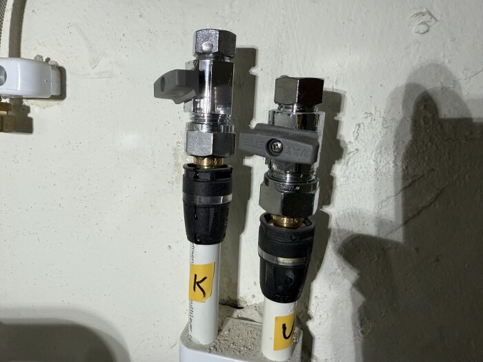 Två vattenrör med märken "K" och "V", kopplade till ventiler där övre muttrar varit hårt fastsatta.
