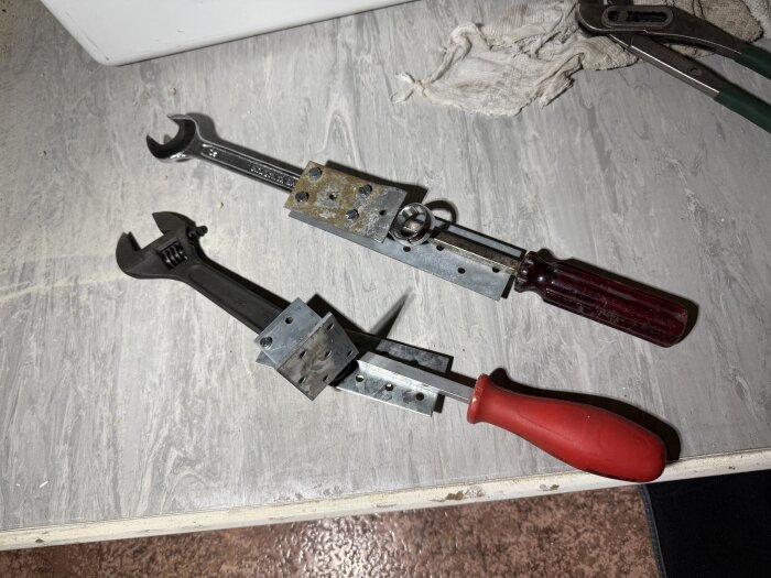 Två skiftnycklar med improviserade hävarmar ligger på en yta, tillsammans med en handduk och andra verktyg.