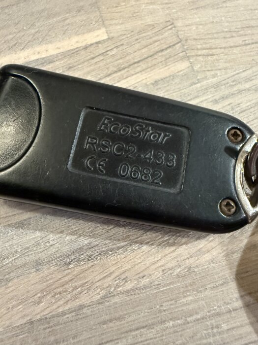 Nyckelbricka med texten "EcoStar RSC2-433 CE 0682" på en träyta.