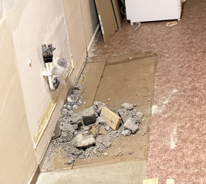 Gammalt avloppsrör synligt efter att material runt omkring knackats bort, visar rör och betong/lös massa på golv i kök från 60-talet.