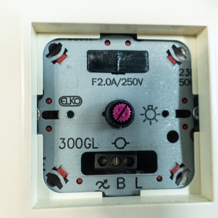 Nära bild på en defekt dimmer från varumärket Elko, märkt med 300GL och 250V, kopplad till ett takljus.
