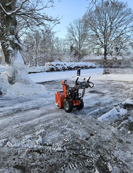 Röd tvåstegs snöslunga med en 205cc motor används för att röja blötsnö på uppfart omgiven av vinterlandskap.