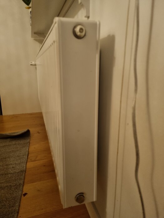 Vitt modernt element monterat på vägg med synliga rör och ventiler, visar problem med ojämn värmefördelning.