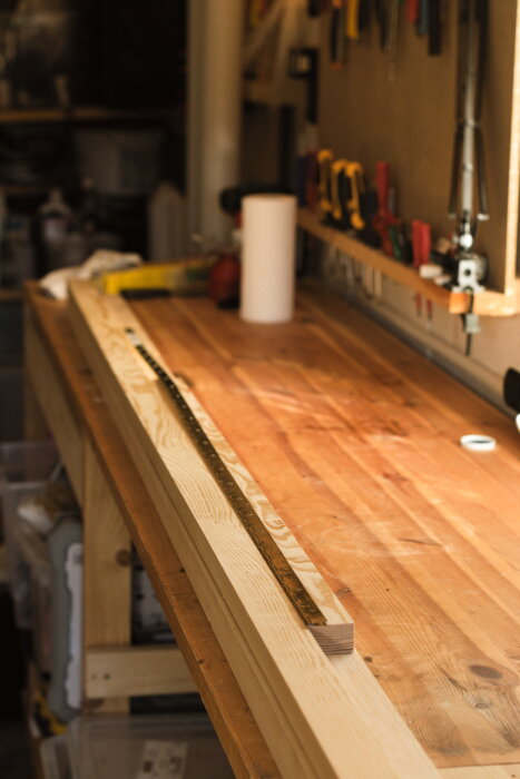 Träskrivbord under konstruktion med pianogångjärn placerat på en arbetsbänk i träverkstad. Verktyg synliga i bakgrunden.