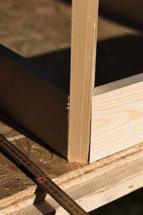 Närbild på hörnet av ett hemmabyggt furuskrivbord med en träregel för mätning på en plywoodyta.