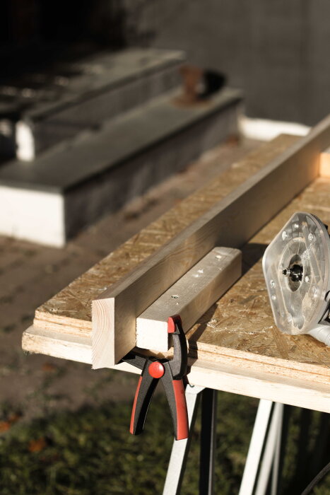 Trästycken fastklämda på en arbetsbänk med en tving, bredvid en fräs, under byggandet av ett skrivbord i furu.
