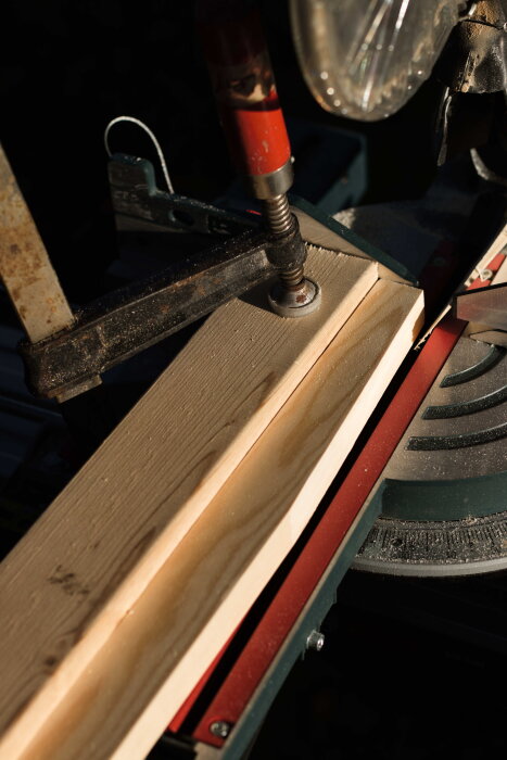 Närbild av en såguppställning med planhyvlat furubräde fastklämt med skruvtving, redo för sågning med kap- och gersåg.