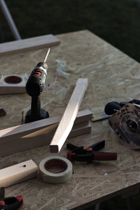 Verktyg och trädelar för skrivbord på arbetsbänk utomhus: borrmaskin, trästomme, fräs och tvingar på plywoodskiva.
