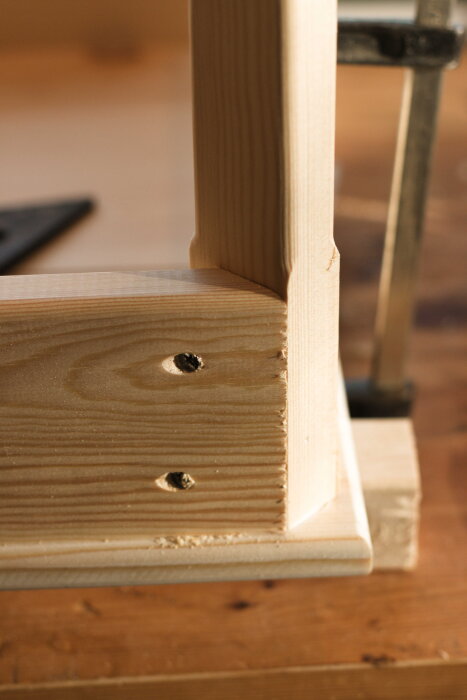 Trädetalj av ett skrivbord i furu med synliga skruvhål och frästa kanter, del av ett hemmabyggt projekt.