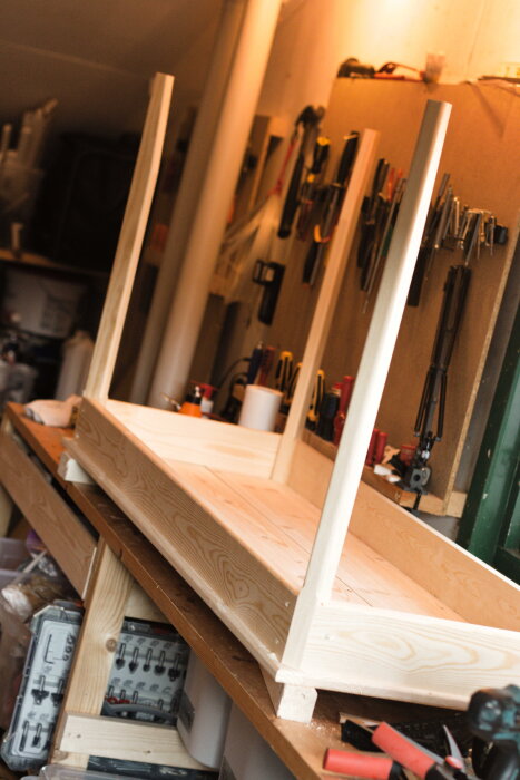 Hemmabyggt skrivbord uppochnervänt på arbetsbänk, med ram och ben i furu, omgiven av verktyg och träarbetesmaterial.