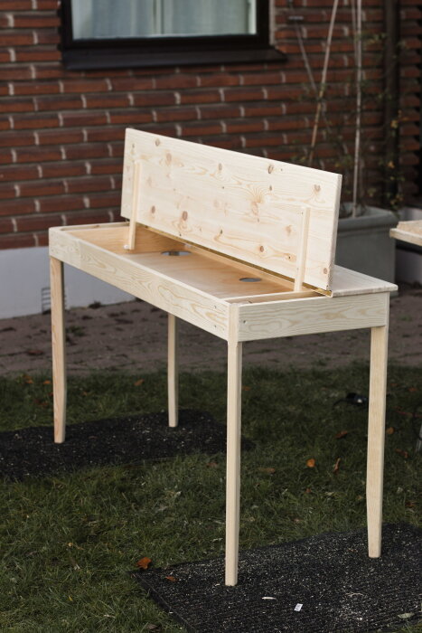 Platsbyggt skrivbord i furu utomhus med öppningsbar topp, konstruerat för att dölja elektronik och utrustat med luftcirkulationshål.
