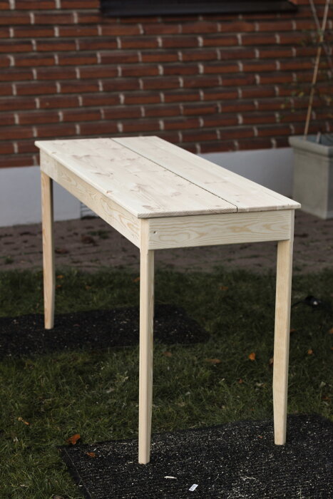 Hemmabyggt skrivbord av furu, stående på gräsmatta. Bordet har frästa kanter och är konstruerat för att gömma datorutrustning.
