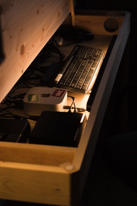 Handgjort träskrivbord med öppen sektion, synlig tangentbord och kablar, samt datorkomponenter under lock.