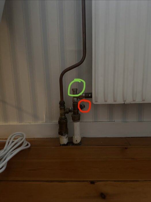 Radiatorrör med en markering i grönt och en i rött vid rörkopplingarna vid golvet och element.