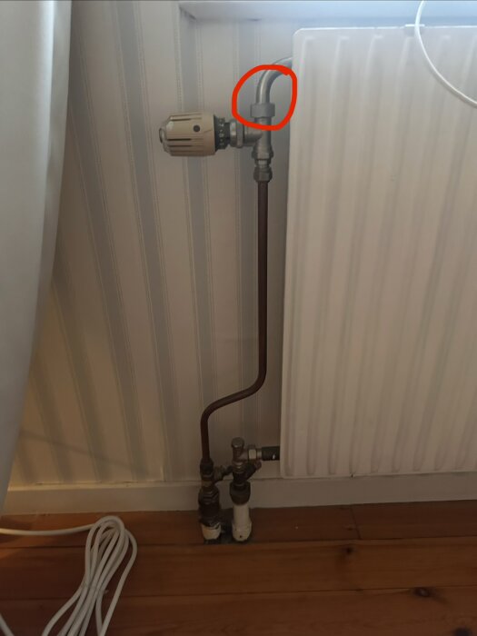 Radiator med termostat, rörsystem, och anslutning markerad med röd cirkel.