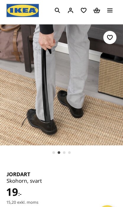 Person använder ett svart skohorn för att ta på sig en svart sko på en matta.