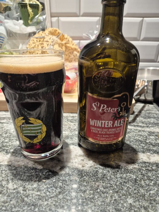 Glas med mörk öl och en flaska St. Peter's Winter Ale på en köksbänk.