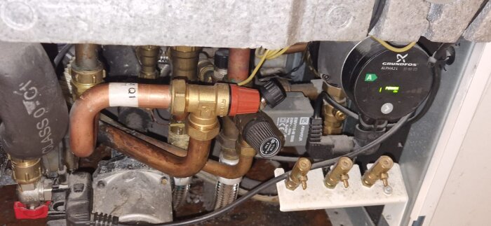 Närbild av rör och ventiler i en Nibe F750 värmepump. Synliga kopparrör, en Grundfos-cirkulationspump och anslutningar i en liten metallisk miljö.