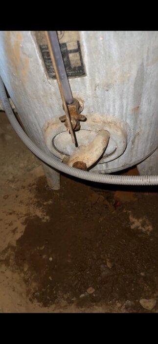 Gammalt och nytt plaströr i anslutning till en metalltank med spruckna rattar, synligt vattenläckage på marken.