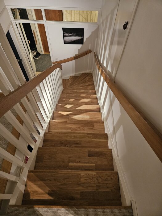 Trätrappa med ljusa väggar och handledare, nylagda trappsteg. Bild inomhus visar trappans konstruktion och dekoration.