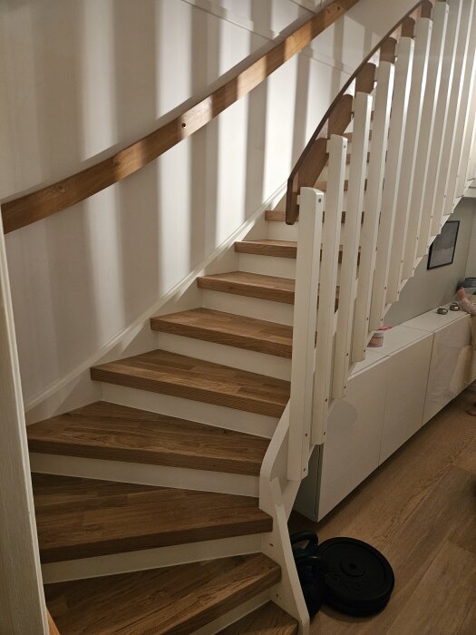 En trappa med trästeg och vit sidolist, nyligen renoverad med fog. En liten glipa syns där ett trappsteg möter listen.