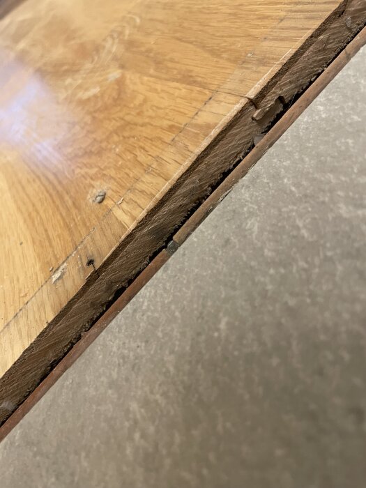 Närbild av ett träparkettgolv med synlig skarv och slitage, i behov av slipning och eventuell behandling.