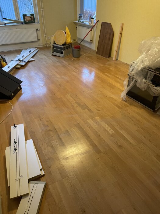 Trägolv i rum under renovering, med verktyg och byggmaterial kring väggarna.