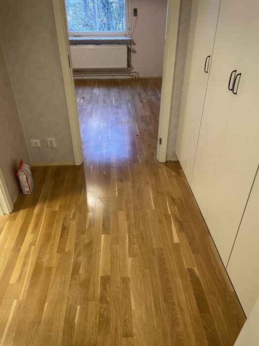 Parkettgolv i en lägenhet, delvis slitna ytor och en tråkig finish, behöver renoveras innan inflyttning. Fönster och garderober syns i bakgrunden.
