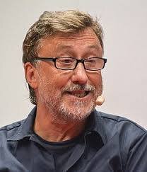 En person med skägg och glasögon ler och har en mikrofon vid kinden.