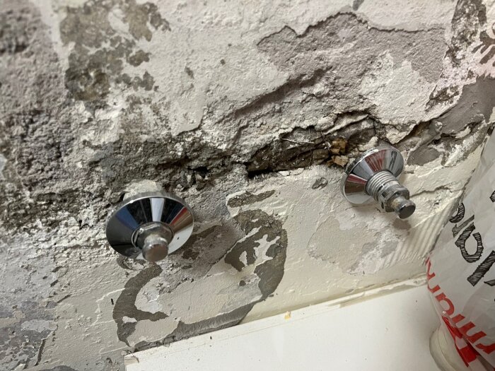 Två pluggade rörstumpar i en köksvägg ovanför diskhon med flagnande färg och rostiga metallproppar.