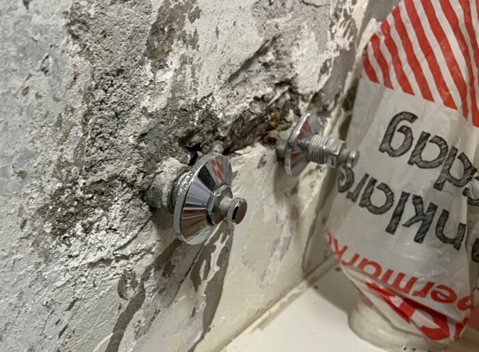 Två pluggade rörstumpar på en vägg med gammalt ytskikt, bredvid en plastpåse, i samband med köksrenovering.