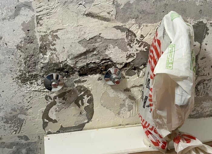 Två pluggade rörstumpar sticker ut ur en vägg med sliten yta, en plastpåse hänger bredvid.