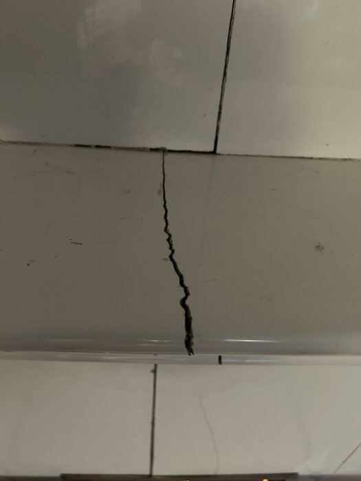 Spricka i kakelugn med synlig skada på glasyren, möjlig reparation efterfrågas.