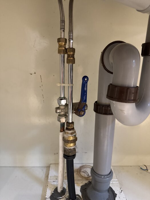 Vattenledningar och avloppsrör under diskho med avstängningsventil i stuga under pågående köksrenovering.