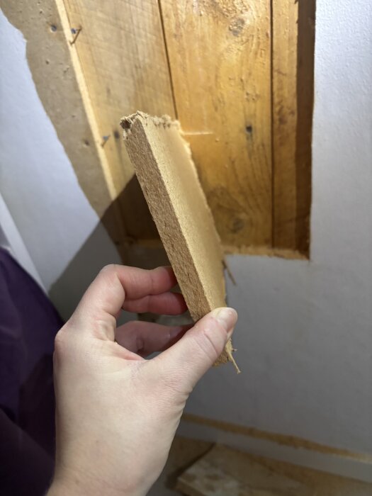 Hand håller en träskiva, potentiellt tretex eller masonit, mot en träpanel från 1957 för identifiering av material.