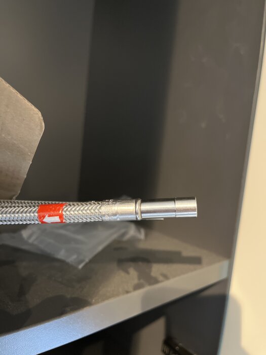 Flätad slang med metallände på hylla, del av byggprojekt.