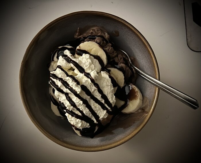 Skål med skivad banan, chokladglass och vispgrädde, toppad med chokladsås.
