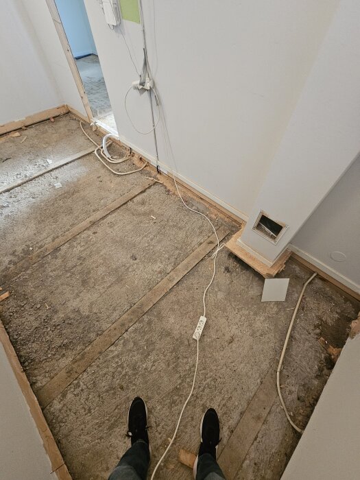 Renovering av golv i sutterängvilla, synliga träbjälkar och kablar längs väggen, del av öppet hål i väggen, trägolv borttaget.