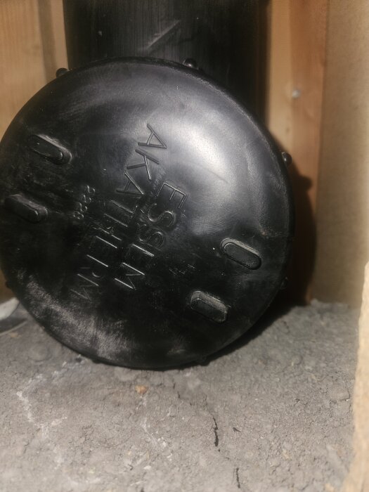 Svart avloppsrör av plast med lock, märkt "AKATHERM", sett inomhus i en byggnad under renovering.