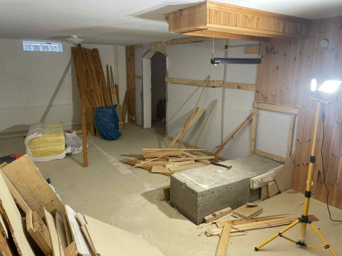 Betongfundament upptäckt vid renovering i källare, omgivet av byggmaterial och träpanel på väggarna. Avslöjades när en barbänk revs.