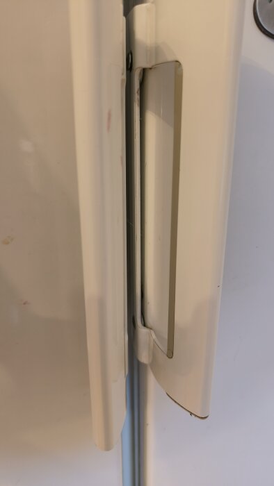 Ett kylskåpshandtag demonterat från en Miele-enhet med synliga skruvar och ersatt med ett stålhandtag från en gammal maskin.
