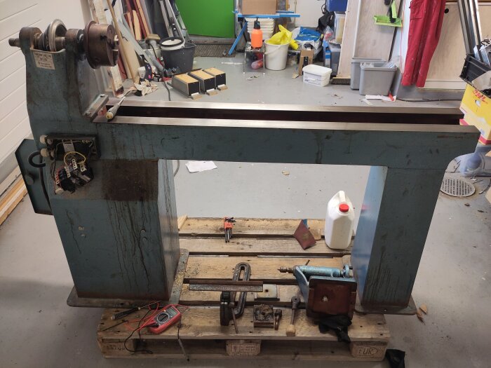 Stor träsvarv står på en lastpall i garage, omgiven av verktyg och diverse föremål.